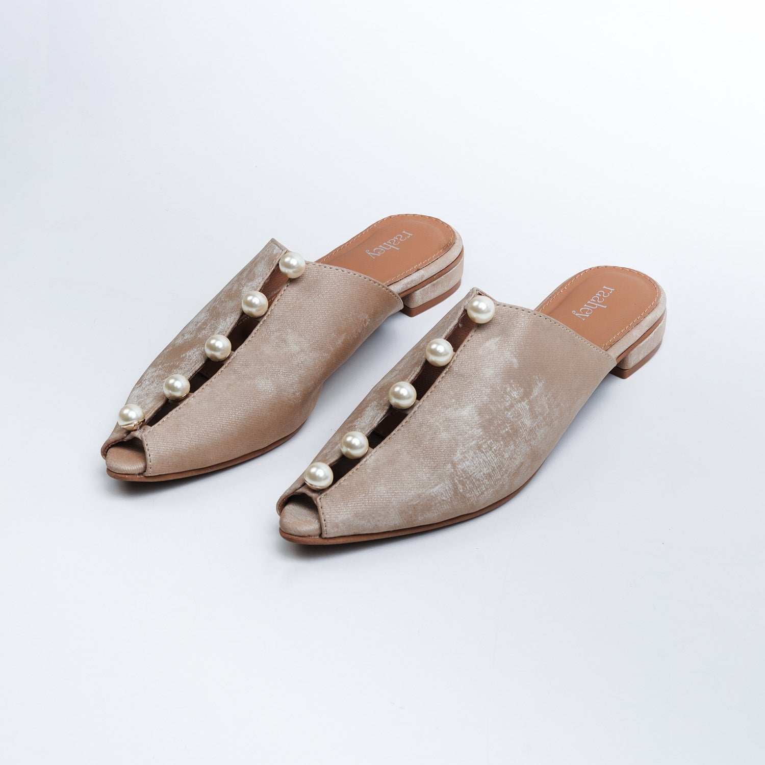 Pair of beige suede mules with pearl embellishments on a white background
